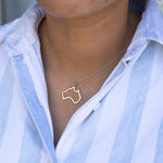 Close-up of a person's neck wearing an  Australia necklace in yellow gold with a blue and white striped shirt against a grey blurred background. 