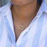 Close-up of a person's neck wearing an  Australia necklace in yellow gold with a blue and white striped shirt against a grey blurred background. 