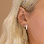 Close-up of a Birthstone Stud - Garnet (January) in white gold and a Horizon Stud in a blonde woman's ear against a light brown background. 