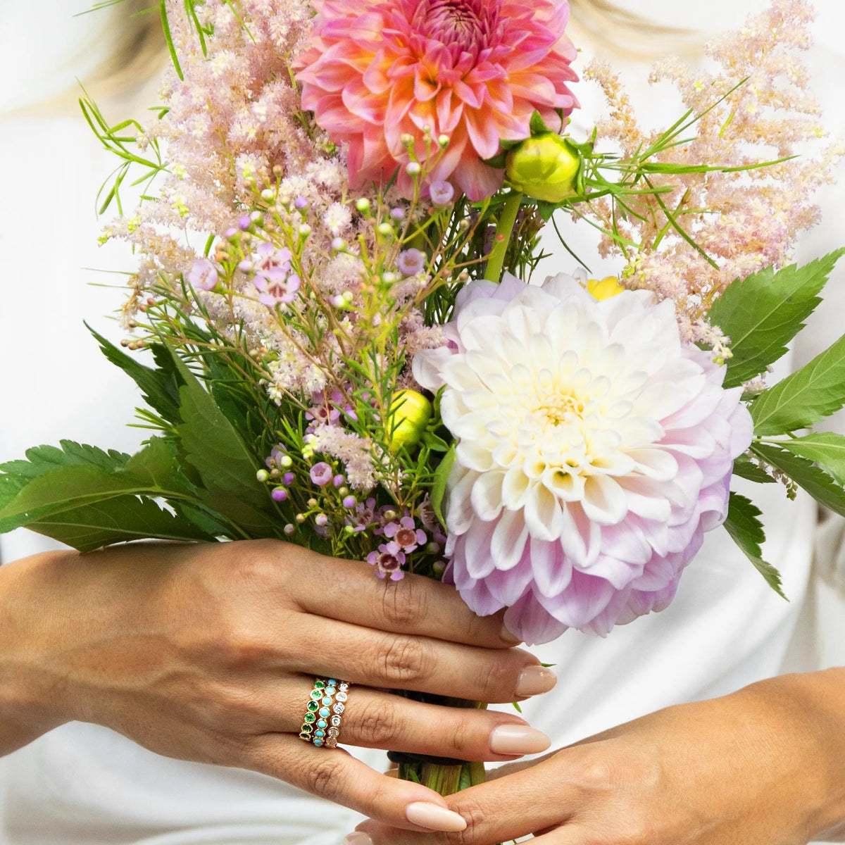 A pair of hands wearing The Fern Bouquet Ring, The Bluebell Bouquet Ring and The Evermore Ring, holding a bunch of flowers. 