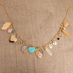 A Box Chain with the following charms - 
20th Anniversary Leaf Pendant, Pink Opal Tear Drop Charm, Turquoise Dangle Charm, Diamond Heart Locket Charm, Abalone Leaf Charm, Moonstone Crescent Charm, Turquoise Heart Charm, Large Abalone Cabochon Charm, two Balance Crystal Charms, Engraved Heart Charm, Small Abalone Cabochon Charm, Onyx Dangle Charm, Cut Out Heart Charm, Opal Dangle Charm and a Heart Locket Charm, against a beige fabric background.