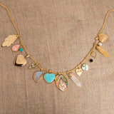 A Box Chain with the following charms - 
20th Anniversary Leaf Pendant, Pink Opal Tear Drop Charm, Turquoise Dangle Charm, Diamond Heart Locket Charm, Abalone Leaf Charm, Moonstone Crescent Charm, Turquoise Heart Charm, Large Abalone Cabochon Charm, two Balance Crystal Charms, Engraved Heart Charm, Small Abalone Cabochon Charm, Onyx Dangle Charm, Cut Out Heart Charm, Opal Dangle Charm and a Heart Locket Charm, against a beige fabric background.