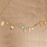 A Box Chain with the following charms - 
20th Anniversary Leaf Pendant, Pink Opal Tear Drop Charm, Turquoise Dangle Charm, Diamond Heart Locket Charm, Abalone Leaf Charm, Moonstone Crescent Charm, Turquoise Heart Charm, Large Abalone Cabochon Charm, two Balance Crystal Charms, Engraved Heart Charm, Small Abalone Cabochon Charm, Onyx Dangle Charm, Cut Out Heart Charm, Opal Dangle Charm and a Heart Locket Charm, against a beige fabric background.
