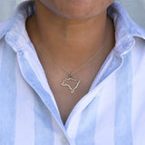 Close-up of a person's neck wearing a Brazil necklace with a blue and white striped shirt against a grey background. 
