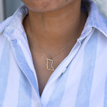 Close-up of a person's neck wearing a British Columbia necklace with a blue and white striped shirt against a grey blurred background. 