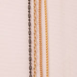 A Black Rhodium Antique Bead Chain, a Round Curb Chain, a Box Chain and a Oval Link Chain laid on an off-white fabric background.