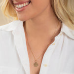 Close-up of a blonde woman wearing a Zodiac Necklace - Capricorn with a white shirt against a neutral background. 