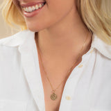 Close-up of a blonde woman wearing a Zodiac Necklace - Capricorn with a white shirt against a neutral background. 