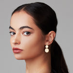 Close-up of a Cascading Solid Eclipse Earring in yellow gold being worn by a women with black hair against a light grey background.