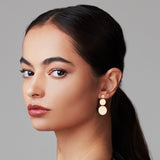 Close-up of a Cascading Solid Eclipse Earring in yellow gold being worn by a women with black hair against a light grey background.