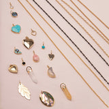 A Box Chain, Black Rhodium Antique Bead Chain, Oval Link Chain, Round Curb Chain,  Opal Dangle Charm, Small Abalone Cabochon Charm, Turquoise Heart Charm,
Cut Out Heart Charm, Diamond Heart Locket Charm, Abalone Leaf Charm, Turquoise Dangle Charm, Pink Opal Tear Drop Charm, Onyx Dangle Charm, Engraved Heart Charm, Heart Locket Charm, two Balance Crystal Charms, Moonstone Crescent Charm, 20th Anniversary Leaf Pendant and a Large Abalone Cabochon Charm against a light pink background. 