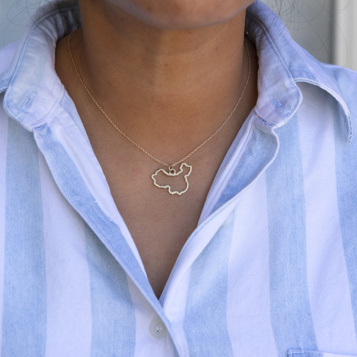 Close-up of a person's neck wearing a China necklace with a blue and white striped shirt against a grey blurred background. 