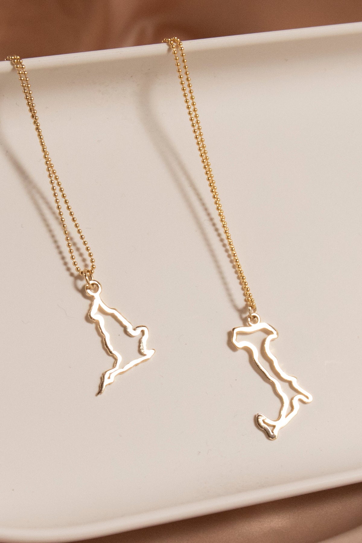 An England Necklace and an Italy Necklace laid on a cream surface against a light brown background.