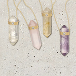 Four The Retreat Necklaces in Clarity, Love, Happiness and Healing on a light grey spotted stone background. 