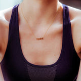 A close-up of a décolletage wearing a FEMME Necklace with a dark purple top. 
