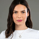 A brunette woman wearing a France necklace and a Tres Pearl Earring in yellow gold with a white knit against a grey background. 