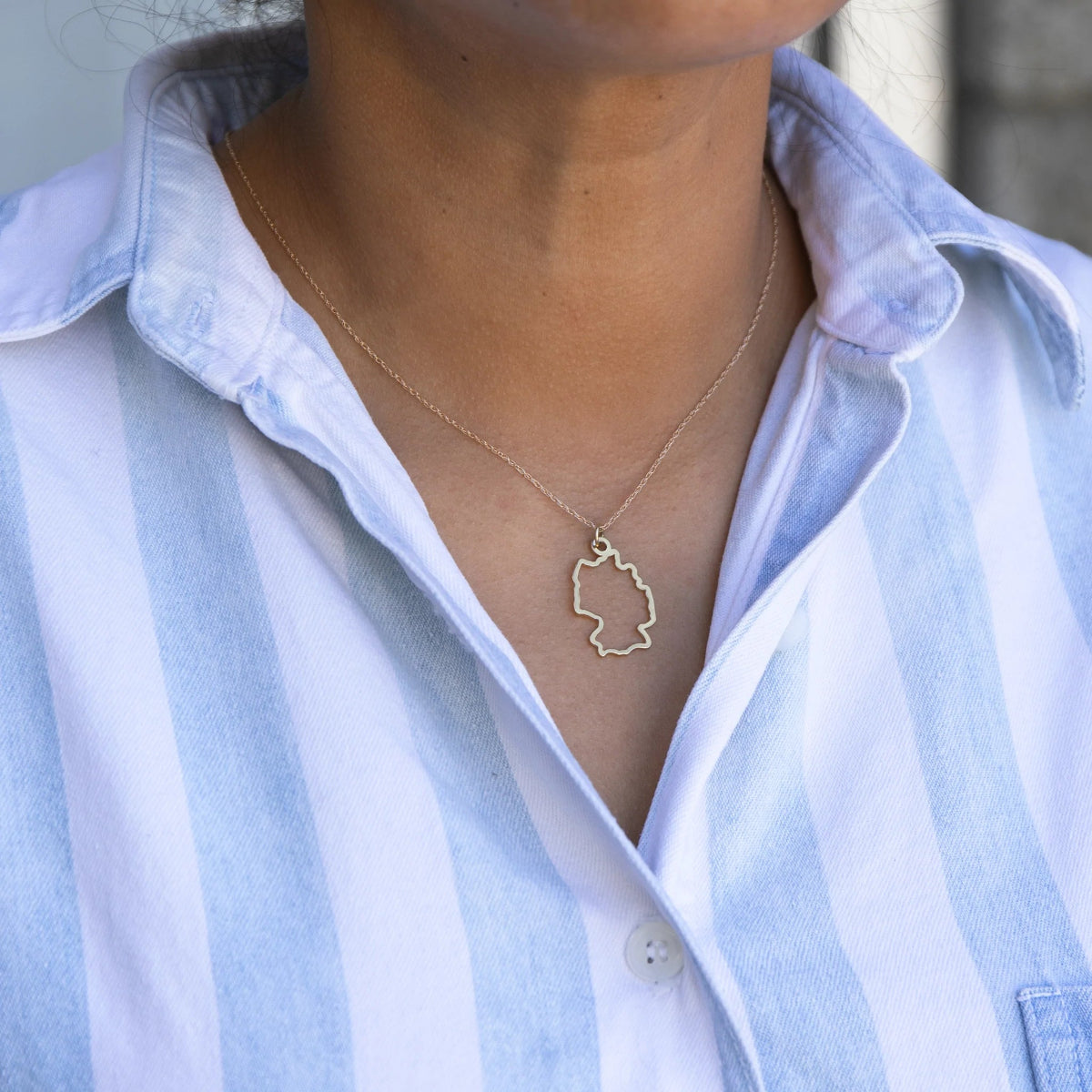Close-up of a person's neck wearing a Germany necklace with a blue and white striped shirt against a light grey blurred background. 