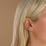 A close-up of a woman’s ear wearing a threader earring with a letter E stud and a star stud earring.