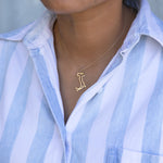 Close-up of a person's neck wearing an Italy necklace in yellow gold with a blue and white striped shirt against a light grey blurred background.