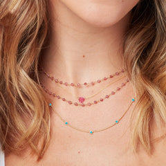 Close-up of a blonde woman's neck wearing a yellow gold Quintet Birthstone Layering Necklace, The Sweetheart Necklace - Pink Sapphire and The Peony Bouquet Necklace. 