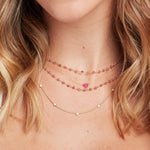 Close-up of a blonde woman's neck wearing a yellow gold Quintet Diamond Layering Necklace, The Sweetheart Necklace - Pink Sapphire and The Peony Bouquet Necklace. 
