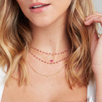 Close-up of a blonde woman's neck wearing a yellow gold Quintet Birthstone Layering Necklace, The Sweetheart Necklace - Pink Sapphire and The Peony Bouquet Necklace. 