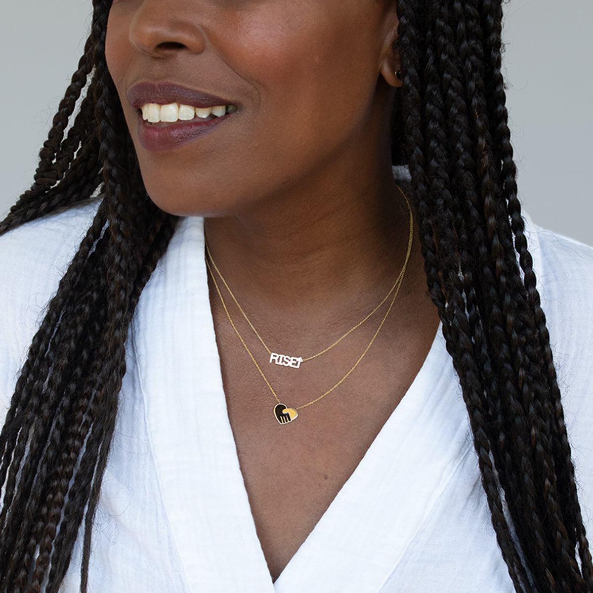 Close-up of a woman wearing a RiseUp Necklace and a Enamel Gold Unity Pendant - Small with a white top against a light grey background. 