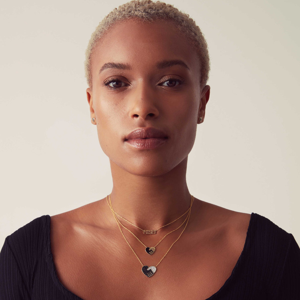 A women wearing Enamel Gold Unity Pendants - Small and Large and a RiseUp Necklace in yellow gold against a light neutral background. 
