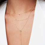 Close-up of a neck wearing a Custom Mixed Gold Necklace - 5 Letter with birthstones, a More Love Necklace and a Gold Lariat Necklace with a white top. 