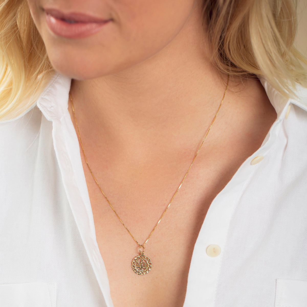 Close-up of a blonde woman wearing a Zodiac Necklace - Libra with a white shirt against a neutral background. 