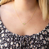 A blonde woman's décolletage wearing a  Lip Pendant necklace with a black top with white flowers. 