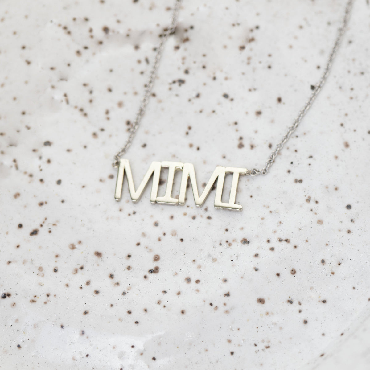 A MIMI Necklace in white gold with a cable chain on a speckled surface. 