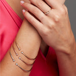 Close-up of a woman’s hand wearing three stacked Doubles Cuffs in yellow gold, rose gold and white gold, a 4 Diamond Ring and a Pavé Diamond Ring, styled in a dark pink top.