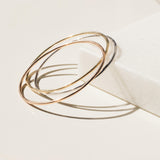 Three Simple Bangles, one in yellow gold, one in rose gold and one in white gold, against an off-white background.