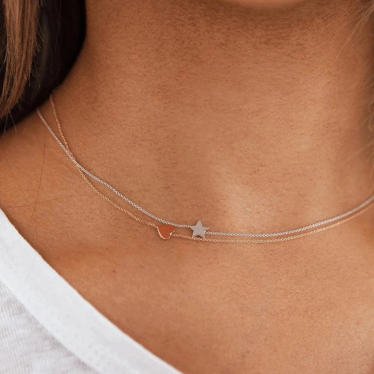 A close-up of a neck wearing two 14k Gold Asymmetrical Charm Necklaces - one heart in rose gold and one star in white gold. 