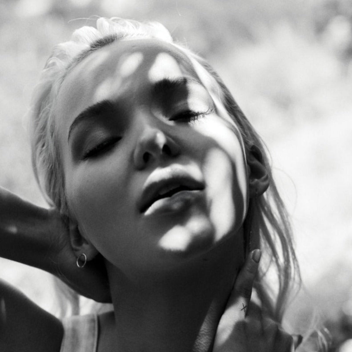 Black and white photo of a woman wearing an Open Eclipse Earring - Small with sunlight casting shadows on her face. 