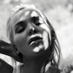 Black and white photo of a woman wearing an Open Eclipse Earring - Small with sunlight casting shadows on her face. 