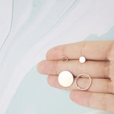 A hand holding an Open Eclipse Earring in Small and Large and a Solid Eclipse Earring in Small and Large, all in white gold, against a light background. 