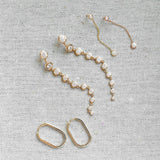 A pair of Oval Hoops, Diamond Cascade Earrings and Droplet Diamond Earrings against a light grey fabric background. 