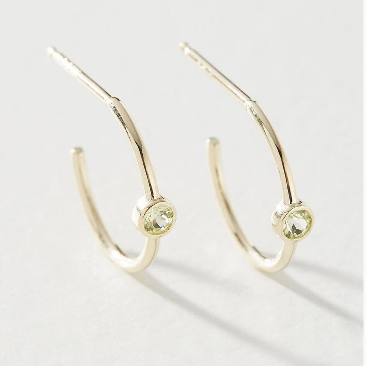 A pair of white gold Birthstone Hoops in August - Peridot against a light grey background. 