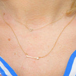 Close-up of a décolletage wearing a 14k Gold Asymmetrical Letter Necklace - R and a Straight as an Arrow Necklace in yellow gold, with a striped blue and white shirt.