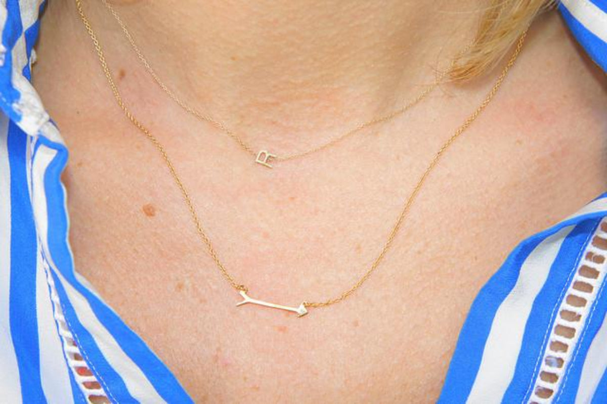 Close-up of a décolletage wearing a 14k Gold Asymmetrical Letter Necklace - R and a Straight as an Arrow Necklace in yellow gold, with a striped blue and white shirt.