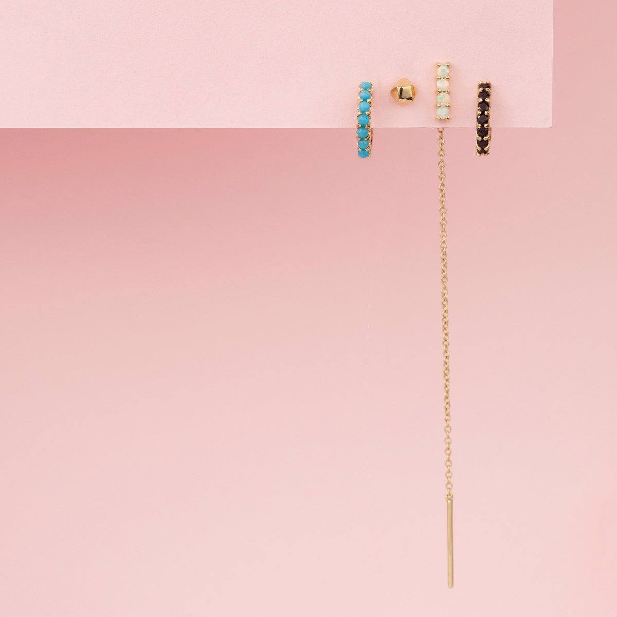 An Alli Webb Turquoise Huggie, Faceted Comfort Stud, Opal Threader and  Onyx Huggie against a light pink background. 