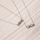 A white gold MIMI Necklace and GAGA Necklace against an off-white fabric background. 