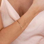 A woman's arm wearing a Straight as an Arrow Bracelet and Doubles Cuff, both in yellow gold, with a light pink silk top. 