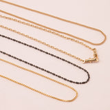 A Black Rhodium Antique Bead Chain, a Round Curb Chain, a Box Chain and a Oval Link Chain laid on an off-white surface. 