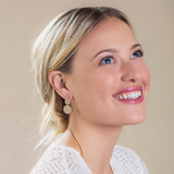 A Cascading Solid Eclipse Earring in yellow gold being worn by a blonde woman looking up in a white top against a light beige background. 