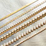 Multiple yellow gold bracelets laid against  a silver metal surface, being an Overboard Bracelet, Bubble Bracelets (Large and Small), a Love Set Match Bracelet and a Down the Line Bracelet. 