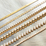 Multiple yellow gold bracelets laid against  a silver metal surface, being an Overboard Bracelet, Bubble Bracelets (Large and Small), a Love Set Match Bracelet and a Down the Line Bracelet. 