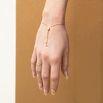 A hand facing down wearing The Slide Heart Bracelet and Delicate Beaded Band in yellow against a tan brown background. 